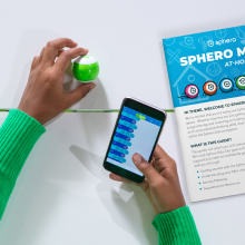 Kid holding Sphero Mini toy robot and phone with block code next to the printed learning guide.