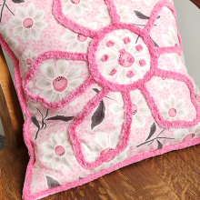 A pink and white quilted pillow with chenille binding